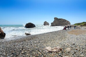 A pebbly beach with large boulders and a clear blue sky. - Villa Nerine by Villa Plus (Peyia)