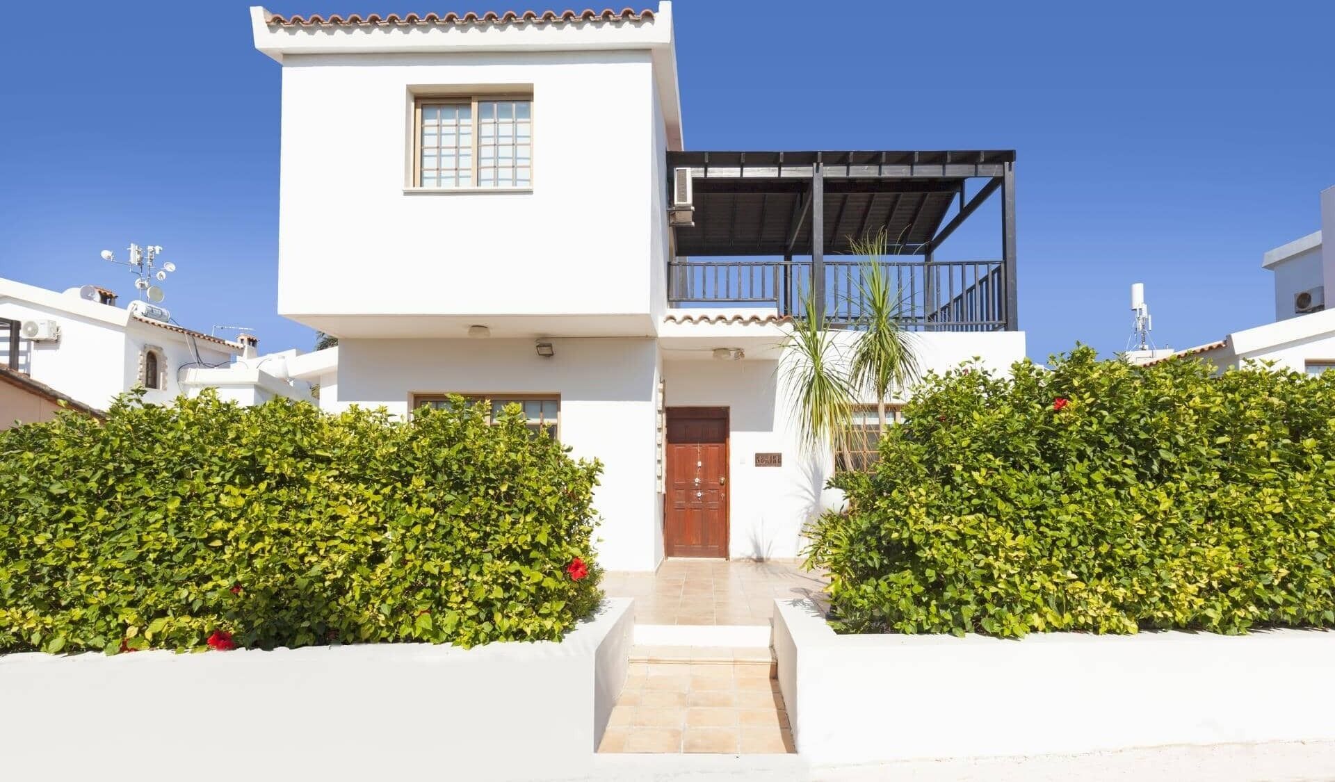 A modern two-story house with a balcony, white exterior, and a small front garden.