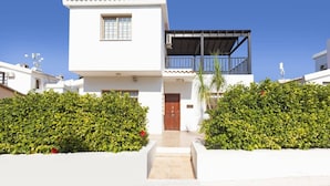 Une maison moderne à deux étages, dotée d’un balcon, d’une façade blanche et d’un petit jardin à l’avant.