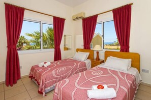 Une chambre d’hôtel avec deux lits, des rideaux rouges, une fenêtre donnant sur un paysage agréable, un miroir et un appareil de climatisation.