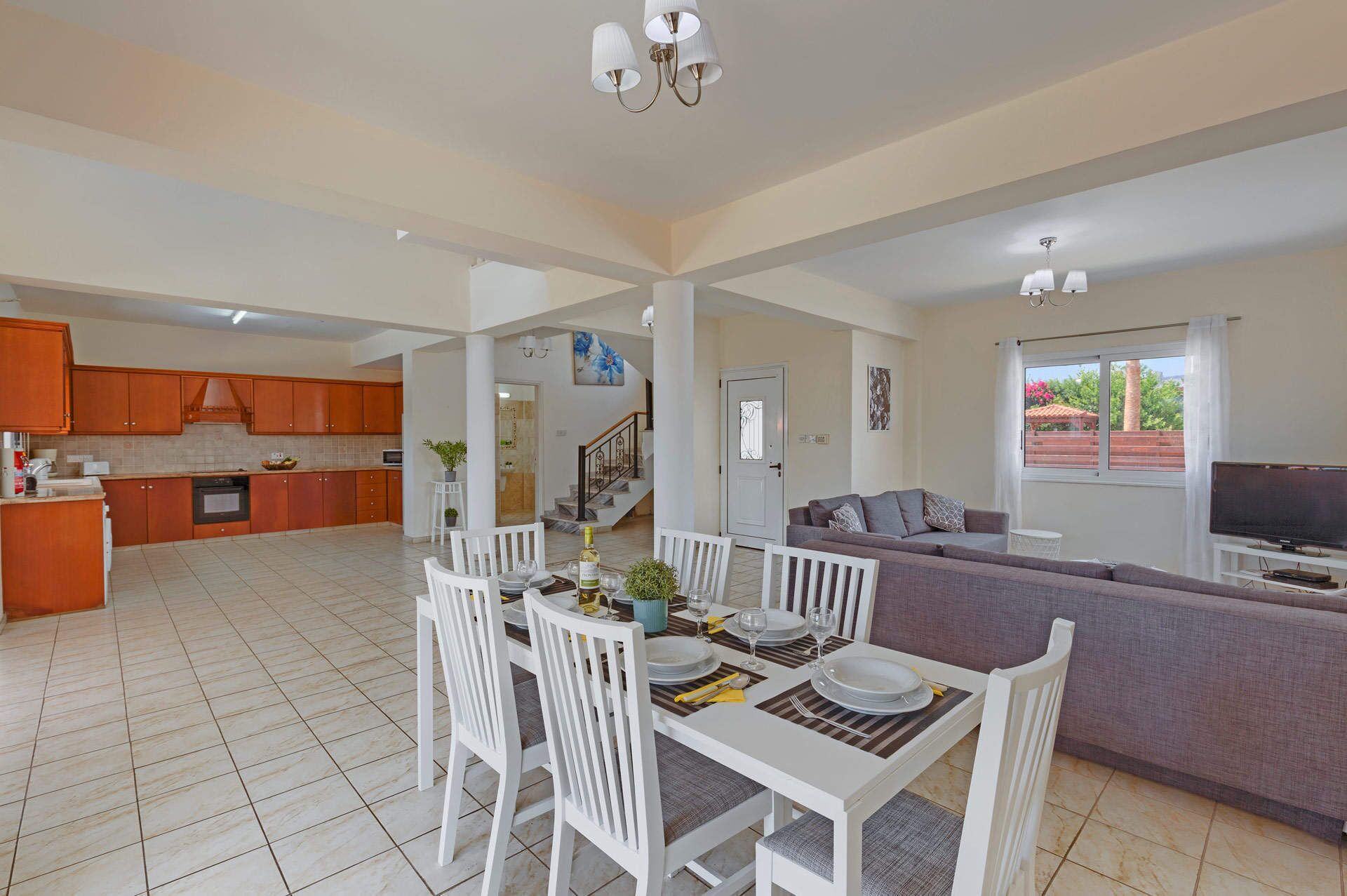 A spacious living area with a dining table set for four, a sofa, and a TV in the background.