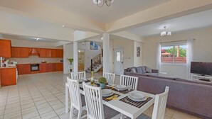 A spacious living area with a dining table set for four, a sofa, and a TV in the background. - Villa Semeli by Villa Plus (Peyia)