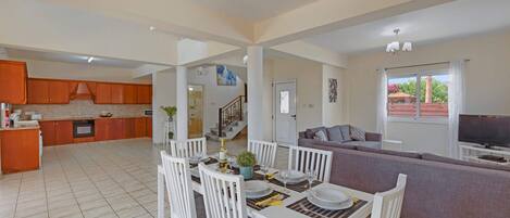 A spacious living area with a dining table set for four, a sofa, and a TV in the background.
