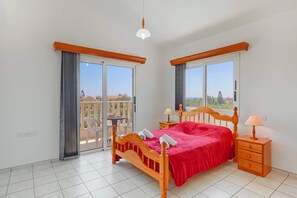 A bedroom with a wooden bed, a nightstand, a table, and a balcony with a view. - Villa Semeli by Villa Plus (Peyia)