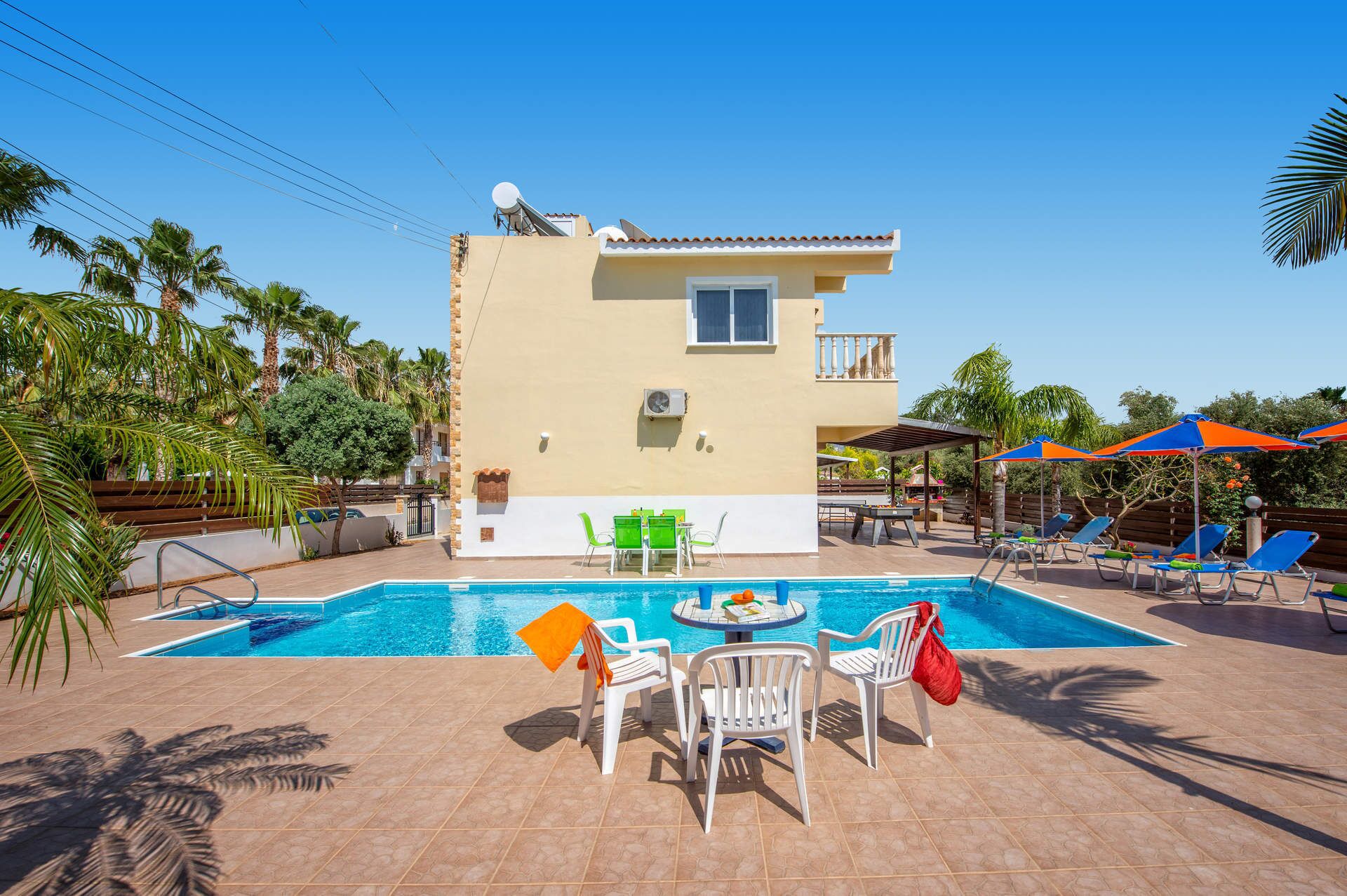 A two-story building with a swimming pool, outdoor seating, and palm trees.
