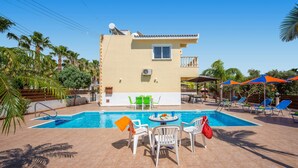 A two-story building with a swimming pool, outdoor seating, and palm trees. - Villa Semeli by Villa Plus (Peyia)