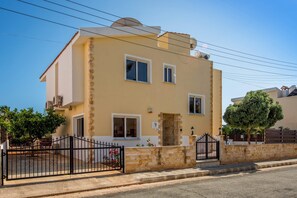 A two-story building with a beige facade, white windows, and a stone wall in front. - Villa Semeli by Villa Plus (Peyia)