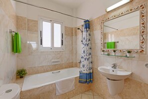 A bathroom with a bathtub, toilet, sink, and a window. - Villa Semeli by Villa Plus (Peyia)
