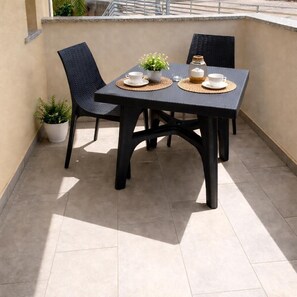 A small outdoor table with two chairs, a potted plant, and a glass jar on a tiled patio. - Beautiful two-bedroom apartment with a pool near the sea in Tropea (Santa Domenica)