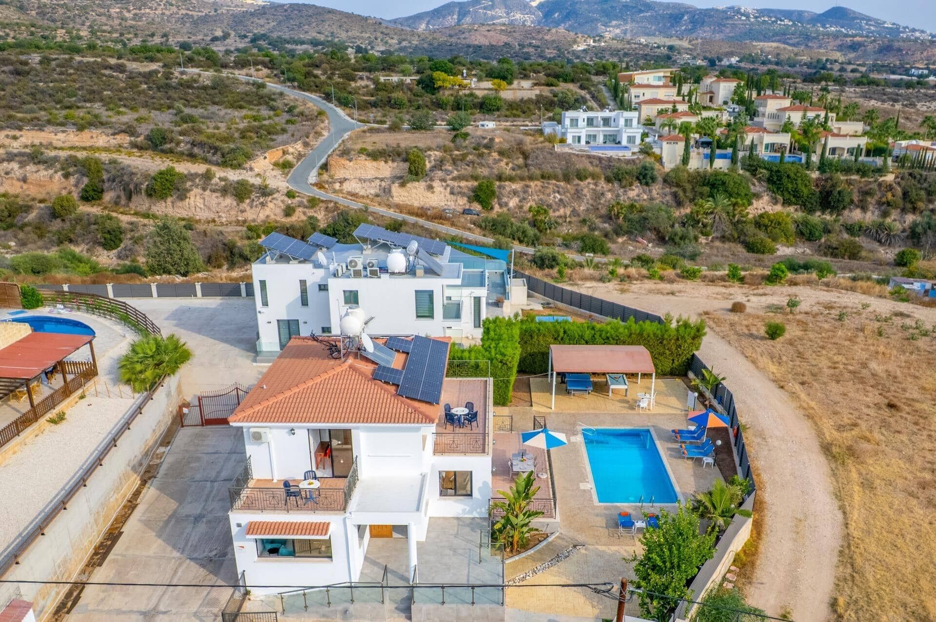 Uma casa moderna de dois andares com piscina, painéis solares e vista para uma paisagem montanhosa.