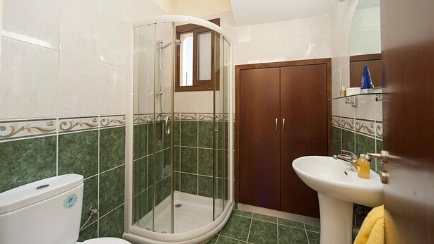A bathroom with a glass shower enclosure, a toilet, a sink, and a wooden wardrobe.
