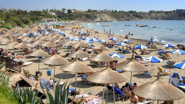 Een strand met veel parasols en ligbedden, een rotsachtige kustlijn en uitzicht op zee.