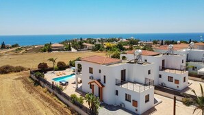 A coastal residential area with white buildings, a swimming pool, and a view of the sea. - Villa Kassiopeia by Villa Plus (Peyia)