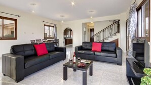 A spacious living room with two black leather sofas, a coffee table, and a staircase leading to an upper floor. - Villa Kassiopeia by Villa Plus (Peyia)