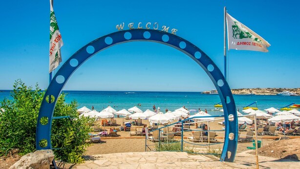 Ein Zugang zum Strand mit einem 'WELCOME'-Bogen, Strandstühlen und Flaggen.