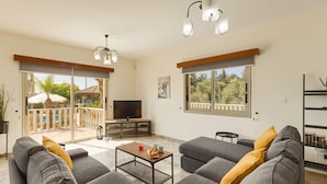 Ein geräumiges Wohnzimmer mit grauen Sofas, einem Couchtisch, einem Fernseher und einem Balkon mit Gartenmöbeln.