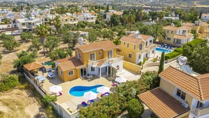 A residential area with houses featuring red-tiled roofs, a central swimming pool, and surrounding greenery. - Villa Frida by Villa Plus (Peyia)