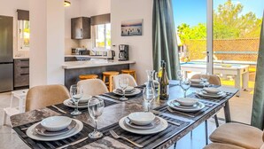 A dining area with a table set for six, a kitchen in the background, and a view of the outdoors. - Villa Frida by Villa Plus (Peyia)