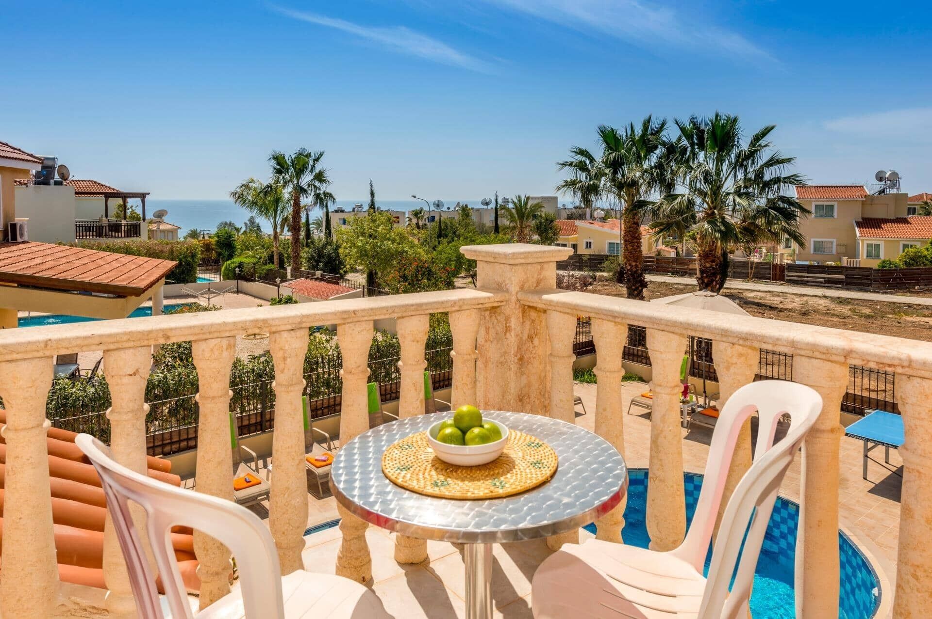 A balcony with a round table, chairs, and a bowl of fruit.