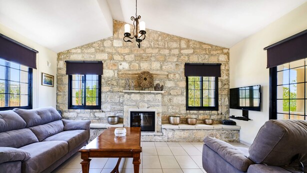 A living room with a stone fireplace, two sofas, a coffee table, and a television mounted on the wall. - Villa Theo Sapphire by Villa Plus (Latchi)