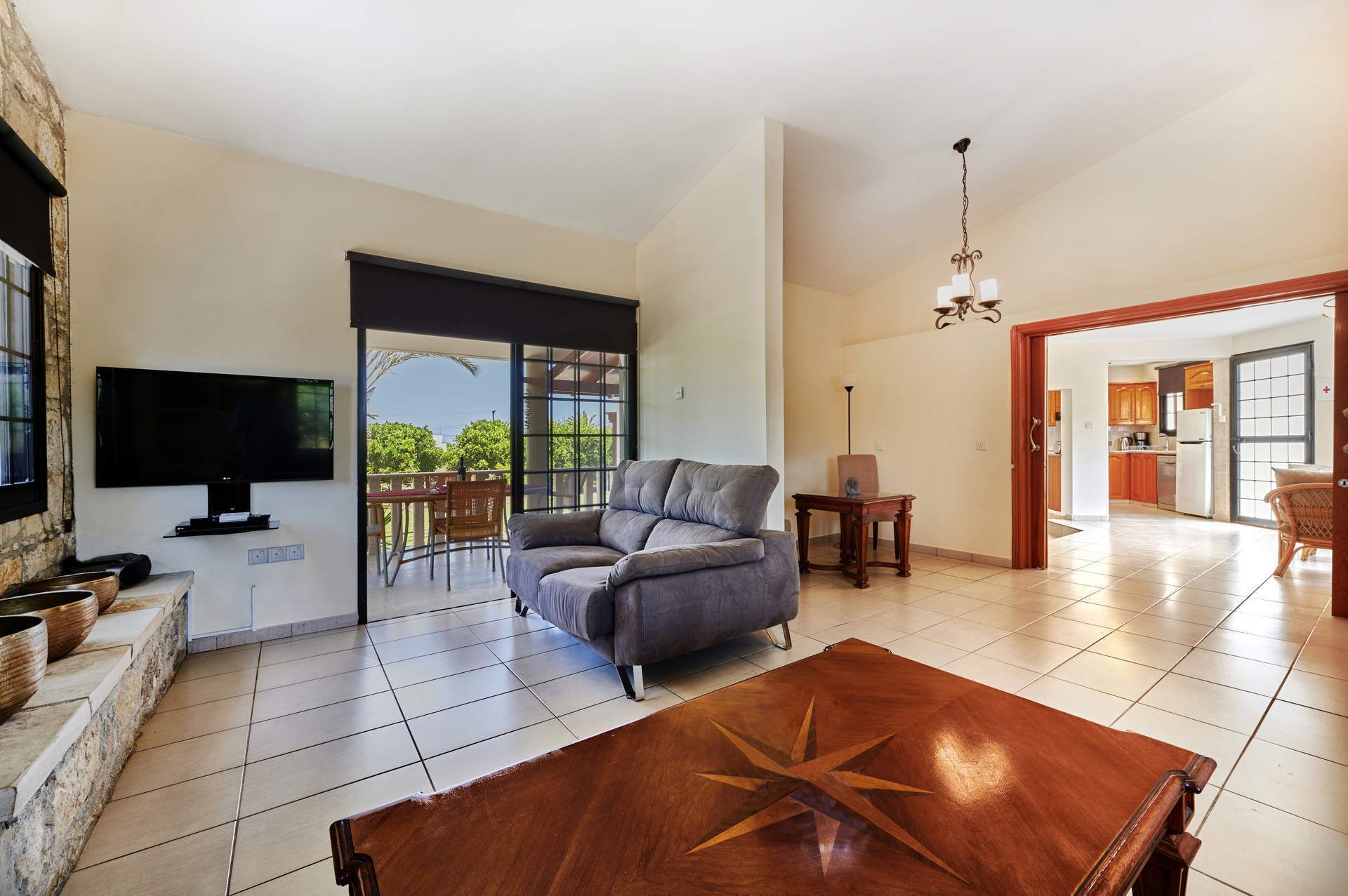 A spacious living room with a flat-screen TV, a grey sofa, and a wooden coffee table with a star design.