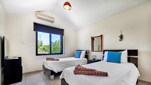 A hotel room with two beds, a large window, an air conditioning unit, a bedside table, a mirror, and a decorative seahorse. - Villa Theo Sapphire by Villa Plus (Latchi)