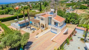 A modern villa with a pool, a covered patio, and a view of the sea.