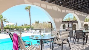 A poolside area with lounge chairs and tables, a clear view of the pool, and a covered seating area with a patterned ceiling.