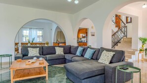 A spacious living area with a large sectional sofa, a wooden coffee table, and a staircase with a metal railing. - Villa Joanna Coral Bay by Villa Plus (Peyia)