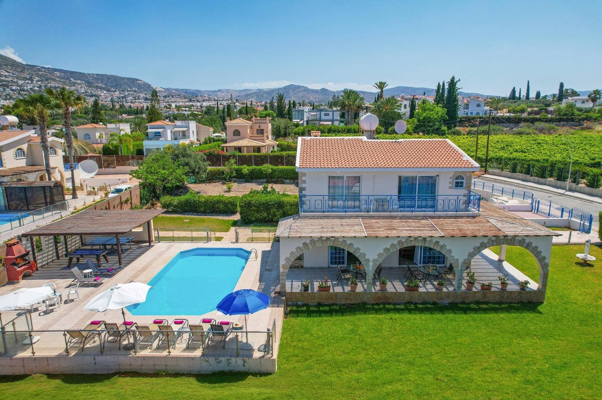 A villa with a swimming pool, outdoor seating, and a view of the surrounding landscape.