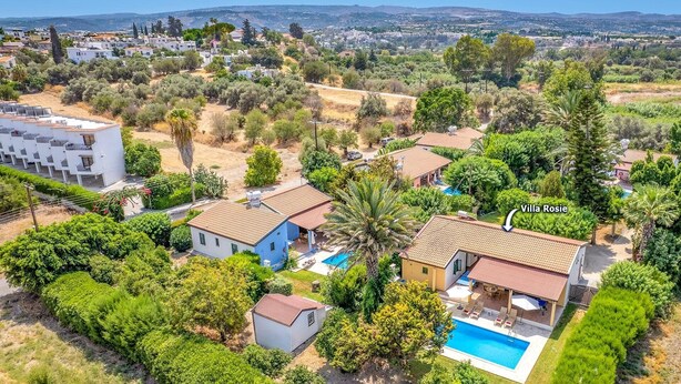 Uma vila com piscina, rodeada por vegetação exuberante e vista para uma cidade ao longe.