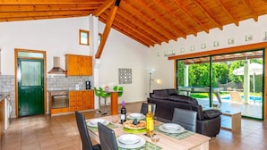 A modern kitchen with wooden cabinets and a dining area with a pool view. - Villa Iriss by Villa Plus (Poli Crysochous)