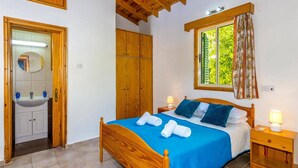 Un dormitorio con cama de madera, dos mesitas de noche, un armario de madera y un baño con espejo y lavamanos.