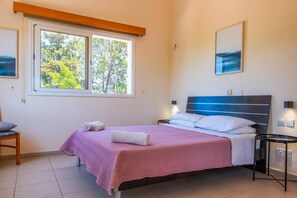 Un dormitorio con una cama, una silla, un ventanal con vistas a árboles y un cuadro en la pared.