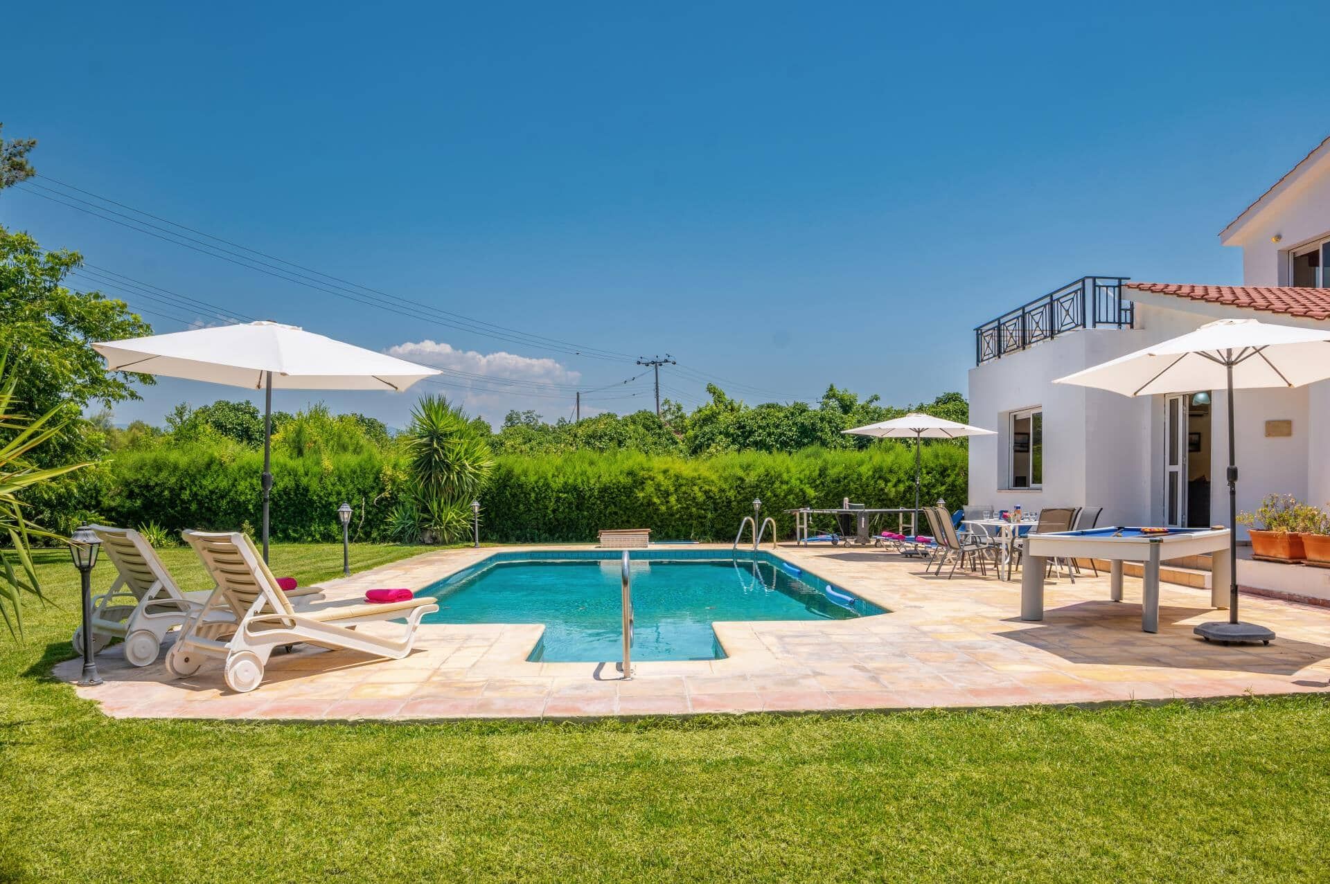 A swimming pool with lounge chairs and umbrellas, surrounded by a well-maintained lawn and a building with a balcony.