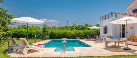 A swimming pool with lounge chairs and umbrellas, surrounded by a well-maintained lawn and a building with a balcony.