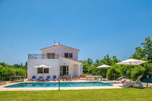 Un edificio de dos pisos con piscina, mobiliario exterior y abundante vegetación.