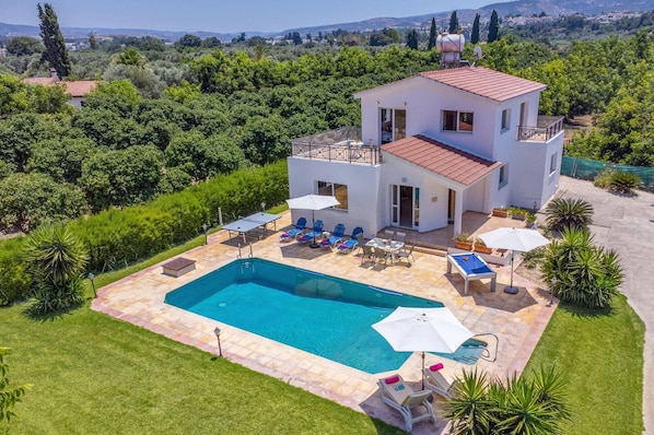 A two-story house with a swimming pool, outdoor seating, and a view of the surrounding landscape.