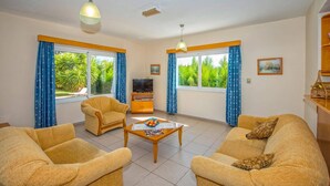Ein Wohnzimmer mit zwei Sofas, einem Couchtisch, einem Fernseher und großen Fenstern mit Vorhängen.