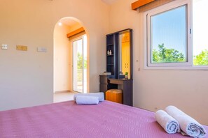 A bedroom with a bed, a vanity with a mirror, a window, and a door leading to an outdoor area.