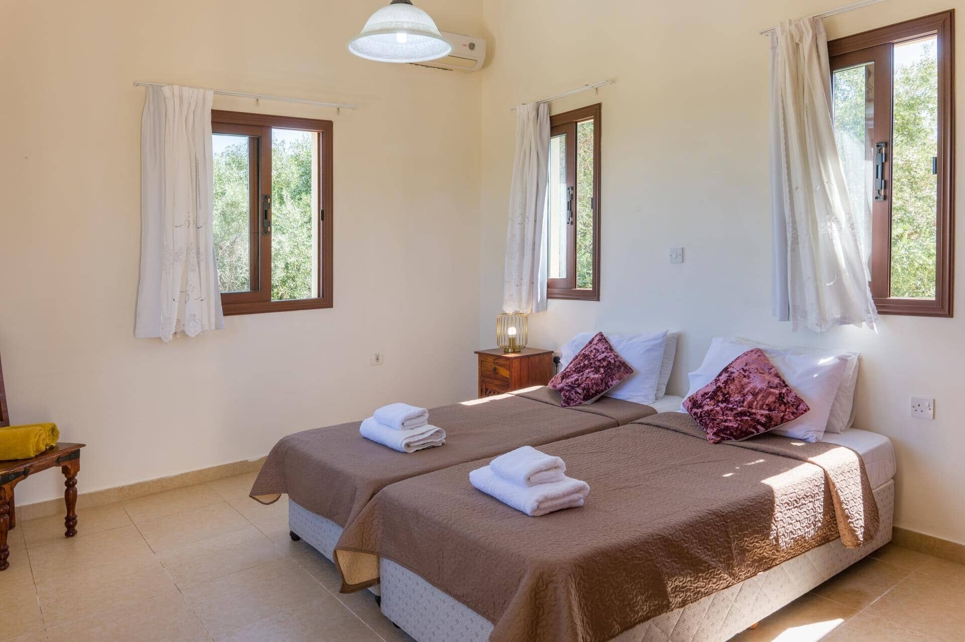 Ein Doppelbett mit zwei Kissen, ein Nachttisch mit Lampe und ein Fenster mit Vorhängen.