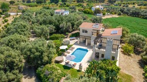 Ein zweistöckiges Haus mit Swimmingpool, umgeben von üppiger Vegetation und Hügeln im Hintergrund.