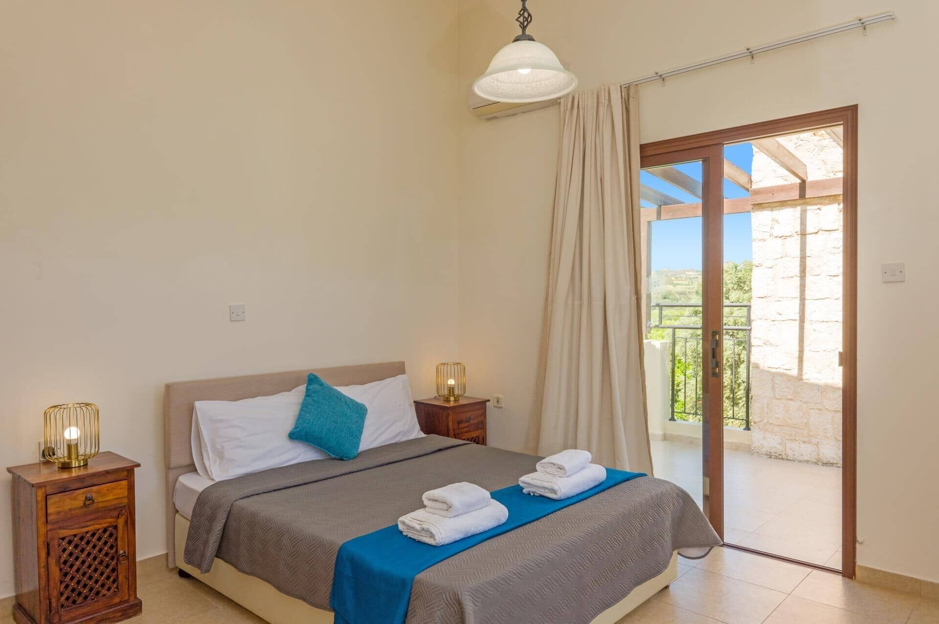 Ein Schlafzimmer mit Bett, Nachttisch, Lampe und Blick ins Freie.