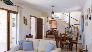 Ein Wohnzimmer mit einer Couch, einem Esstisch und Stühlen. Eine Treppe führt zu einer weiteren Ebene.