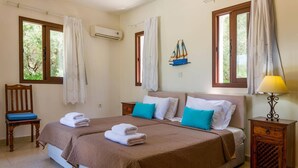 Quarto com cama, duas mesas de cabeceira, uma cadeira e janela com cortinas.