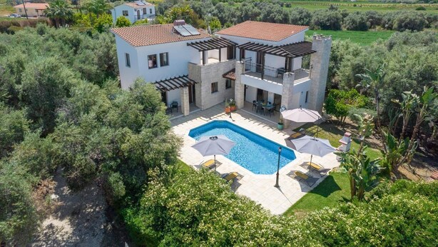 Uma casa de dois andares com piscina, rodeada por vegetação e colinas.