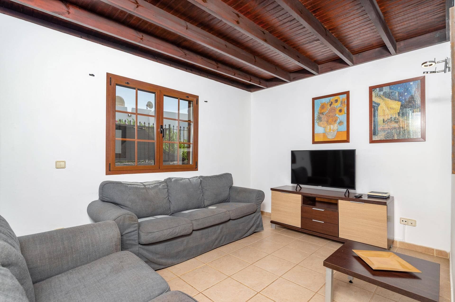 A living room with a grey sofa, a TV, a wooden cabinet, and two framed artworks on the wall.