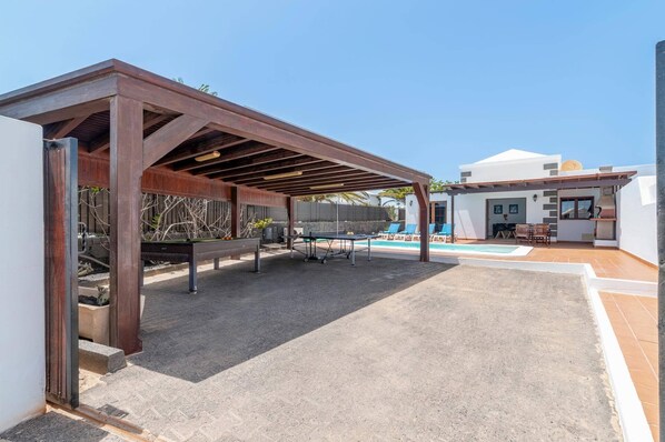 A covered outdoor area with a pool, lounge chairs, and a barbecue grill. - Villa Siroco Lanzarote by Villa Plus (Playa Blanca)