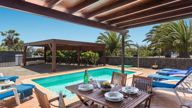 Un espacio al aire libre techado con piscina, sillas de descanso y una mesa lista para comer.