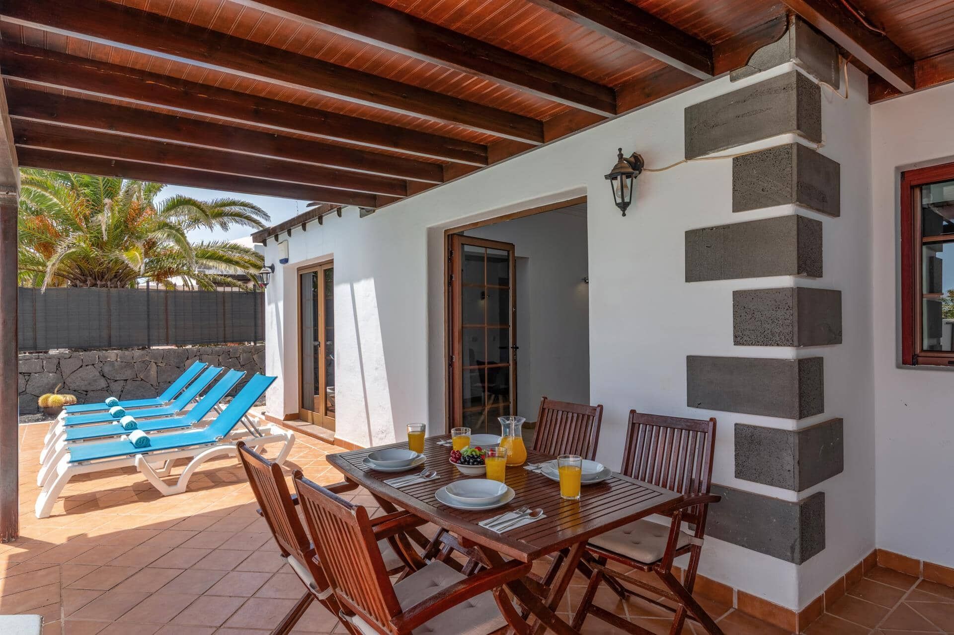 An outdoor patio with a wooden table set for dining, surrounded by blue lounge chairs.